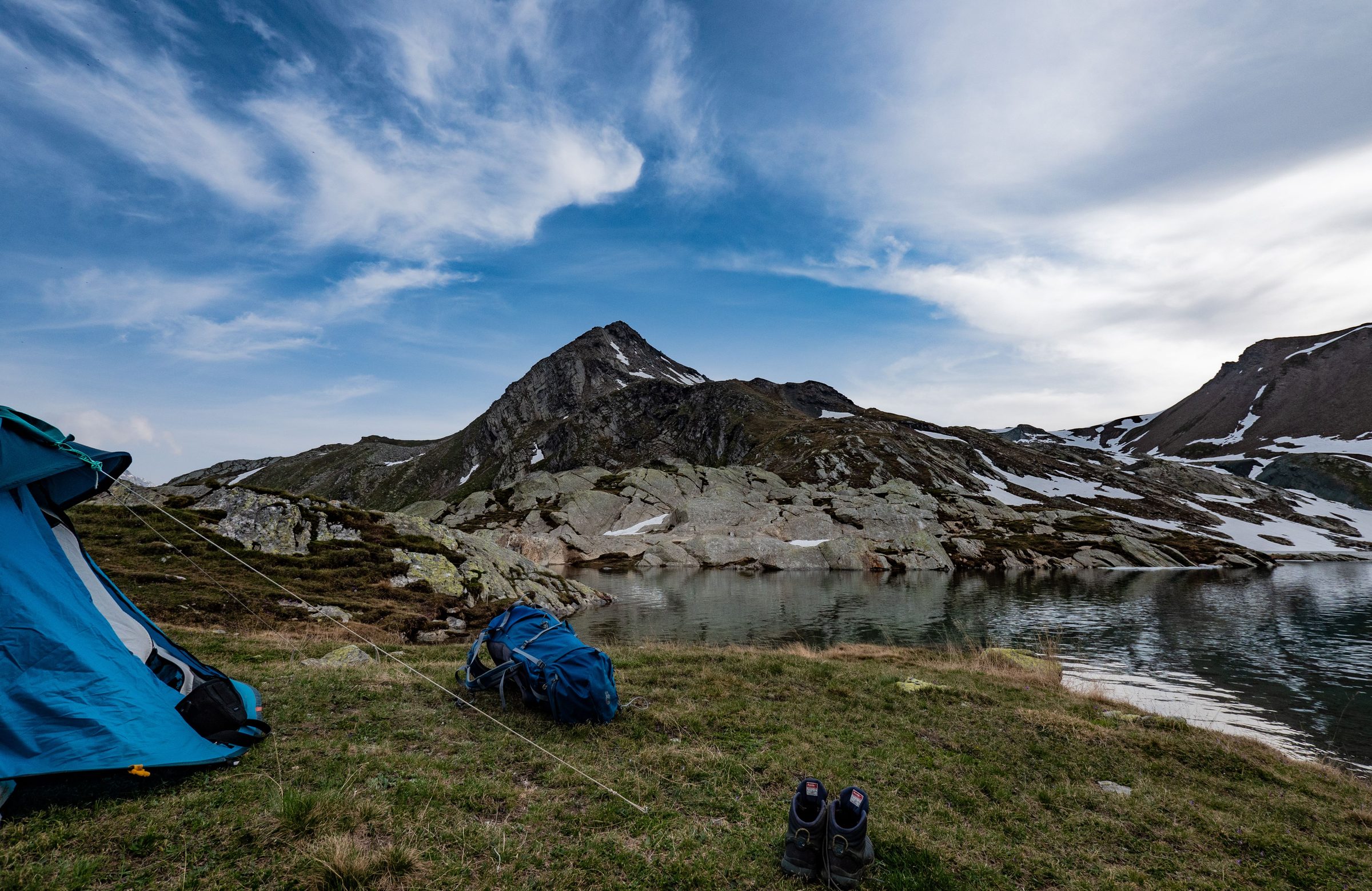 Blue tent, backpack and boots beside an alpine tarn