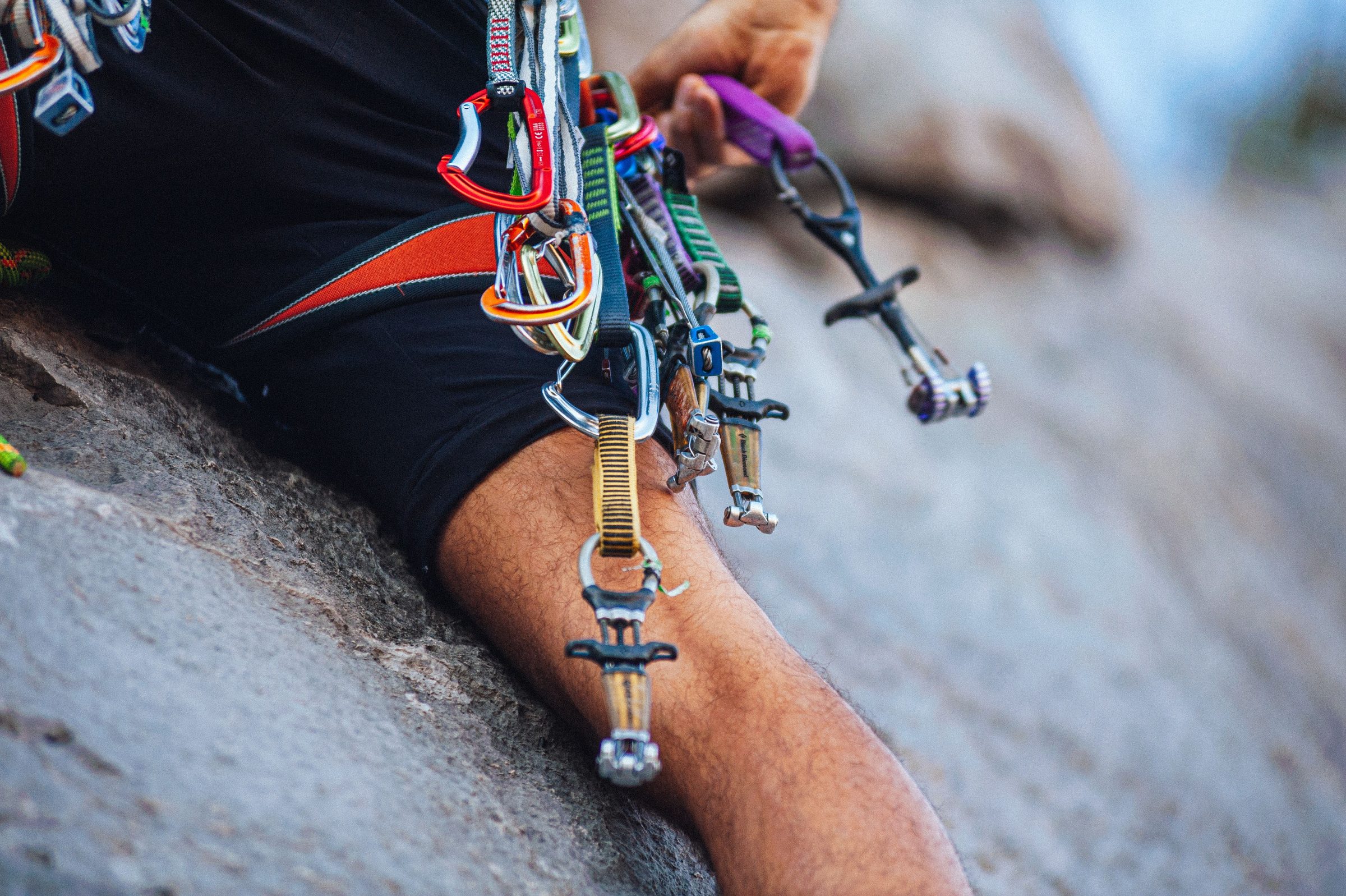 Cams and carabiners racked on a climber's harness against granite
