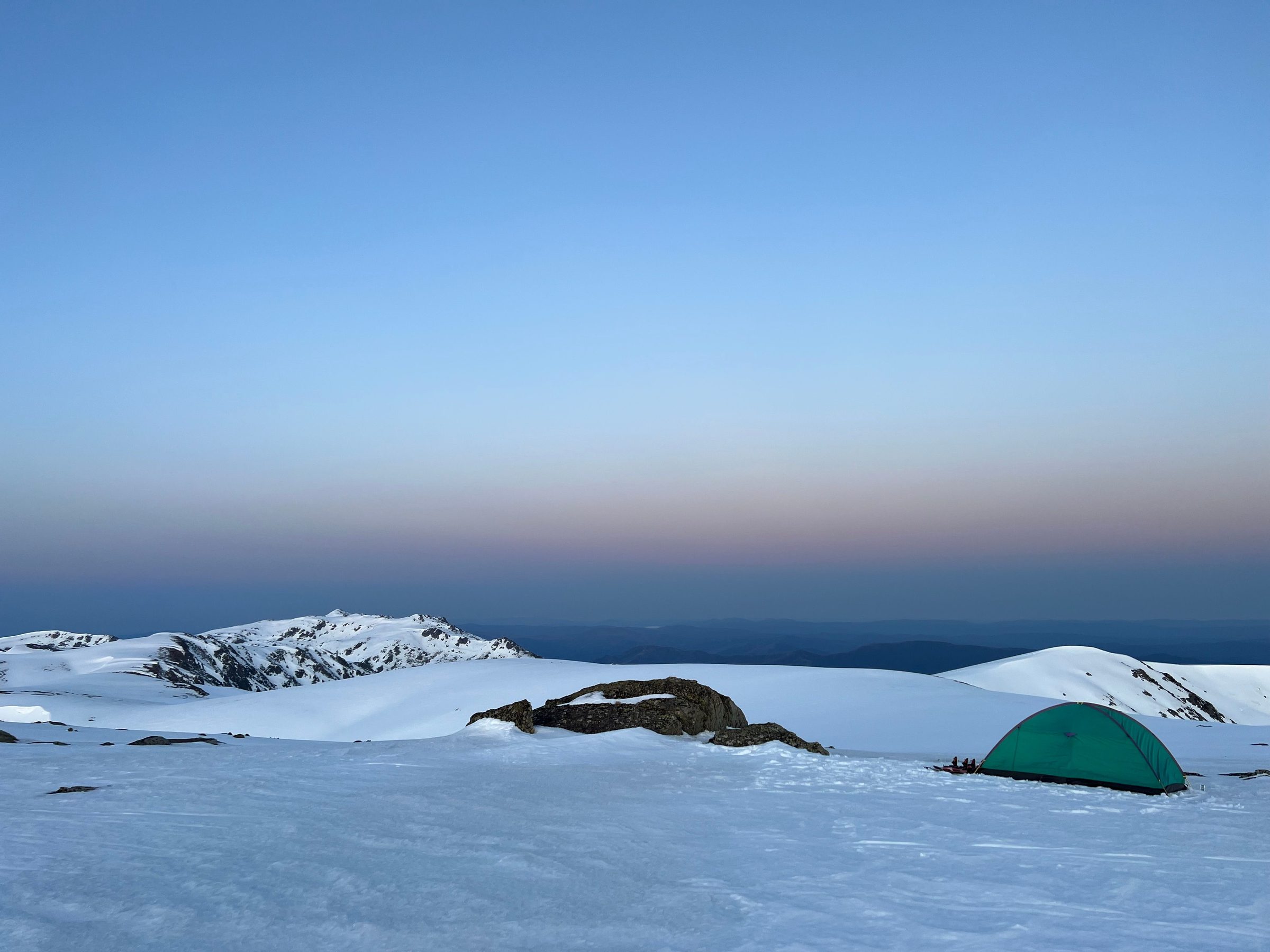 Green tent on a snowfield at dusk
